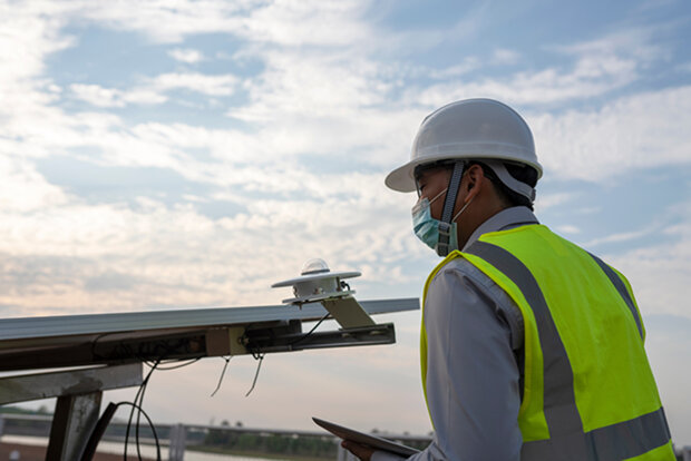 Person in a hard hat next to a solar panel and a small instrument with a glass bubble on top